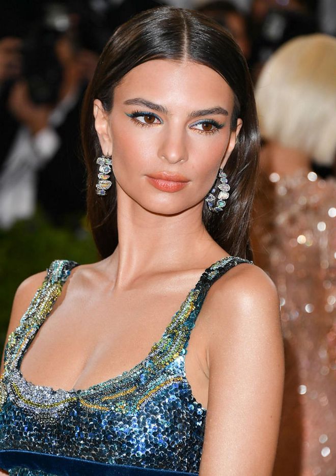 Turquoise and coral lined eyes. Sheer tangerine lips. A sun kissed glow. Emily Ratajkowski brought about the beauty of a sunset by the Santorini with this beauty look (Photo: Getty)