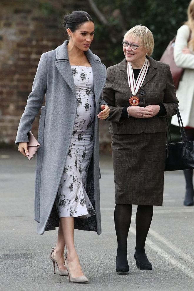 the Duchess of Sussex wore a gray wool coat by Canadian brand Soia & Kyo with a midi-length floral dress by coveted brand, Brock Collection.  For accessories, she went simple with Aquazzura suede pumps (one of her go-tos), a silk fold-over clutch by Wilbur & Gussie, and tear-drop shaped Maison Birks earrings.