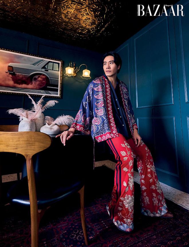 Hong relaxes in his dining room in a Gucci kimono and trousers, shirt from Beyond The Vines, Maison Margiela boots, and Mia Jasmine ring (worn throughout). On the wall behind him are lamps which were formerly from the storied Raffles Hotel