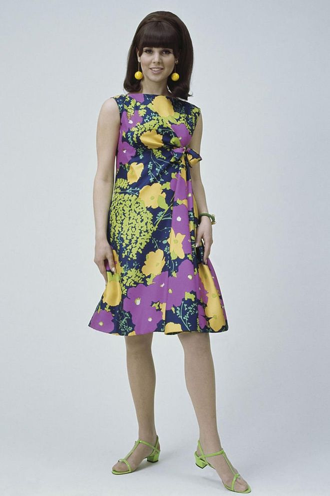 A model shows off a colourful print dress, yellow pom-pom earrings and neon green heels while on set. Photo: Getty 
