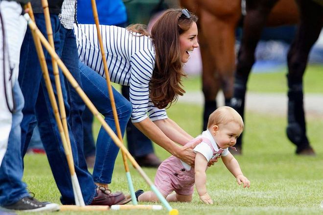 Duchess Kate plays with baby Prince George in the grass while they watch Prince William play in a charity polo match. Photo: Getty