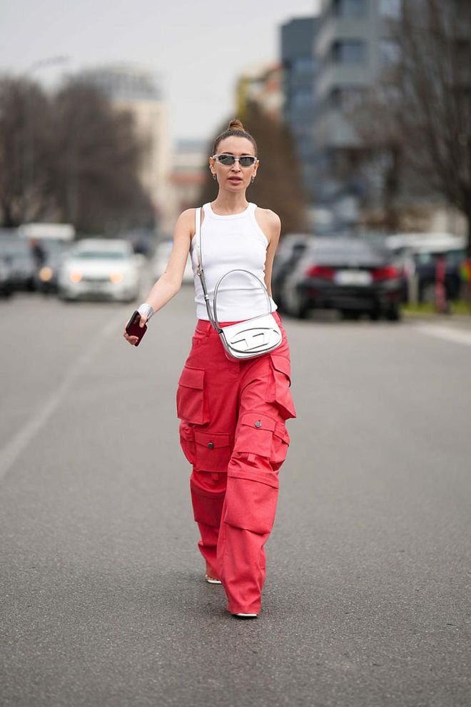 MILAN, ITALY - FEBRUARY 23: A guest wears silver sport sunglasses, a white halter neck tank-top, a silver shiny leather crossbody bag fro Diesel, red large cargo pants, white shiny leather heels sandals , silver large bracelets , outside Prada, during the Milan Fashion Week Womenswear Fall/Winter 2023/2024 on February 23, 2023 in Milan, Italy. (Photo by Edward Berthelot/Getty Images)