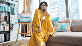 Perched on her living room sofa in front of a painting by her grandfather, Kausar is dressed in traditional wide-legged gharara trousers paired with a kurta, a sat lara necklace and earrings gifted by her in-laws on her first visit to India, together with SunMoonRain bangles, and embroidered traditional shoes from Pakistan