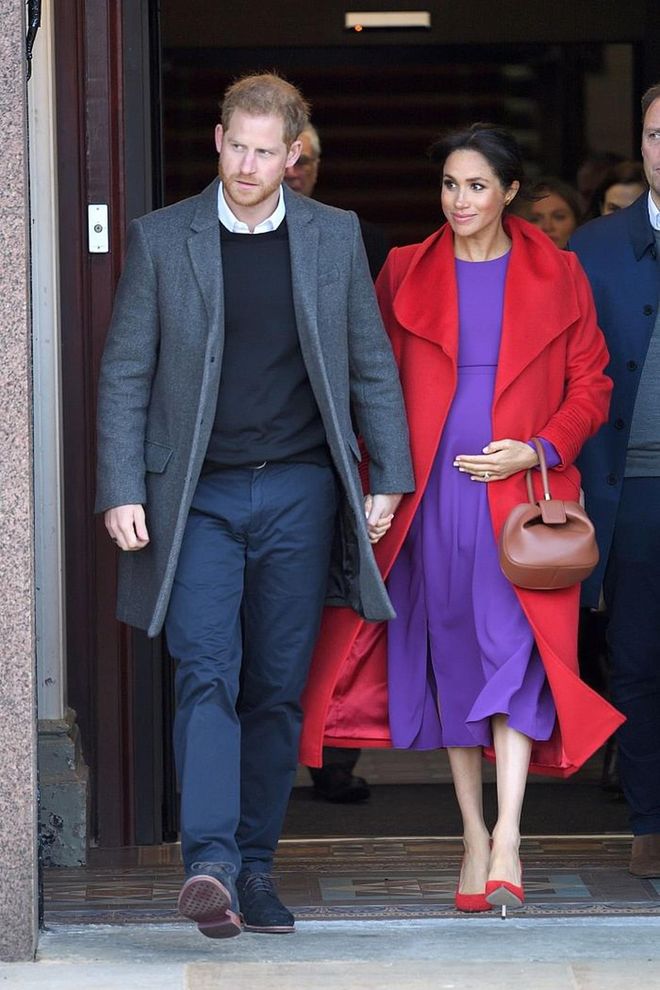 The Duchess of Sussex visited  Hamilton Square wearing brights! She wore a violet Babaton 'Maxwell' Dress under a vibrant red custom coat by Sentaler. The Duchess accessoried this Spring look with red Stuart Weitzman pumps and a tan Gabriela Hearst 'Nina' bag.   