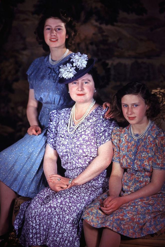 A young Queen Elizabeth II and Princess Margaret pose with Queen Elizabeth the Queen Mother. The mother-daughter trio sport floral '40s-style dresses and matching pearls for the portrait.