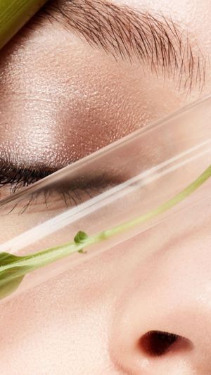 close up beauty shot of a female face that has test tubes filled with green smoothie and leafy plants in it- symbolizing organic make-up and natural beauty treatment