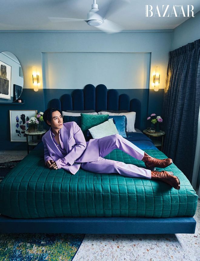 Hong wears a BOSS pantsuit and boots from Maison Margiela as he lounges on his bed with its scalloped headboard which was a deliberate choice, along with the organically-shaped mirror, to contrast with the square layout of the bedroom.