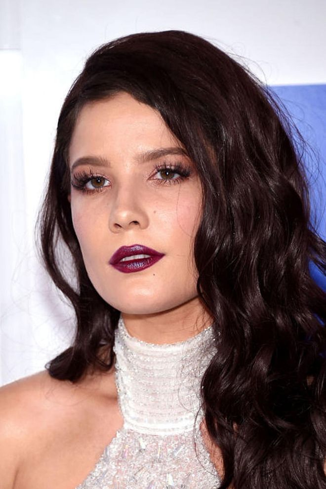 The singer trades in her signature cropped 'do for what appears to be a chocolate brown wavy wig. She punctuated the look with a dark purple lip.