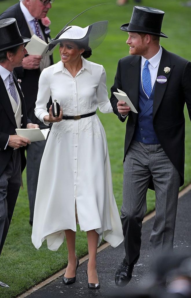 The Duchess of Sussex attends her first Royal Ascot in a bespoke white shirt dress by Givenchy, with a lace design at the waist. She accessorized with a black and white hat from Philip Treacy's SS18 collection and a Givenchy black satin clutch and leather pumps. 