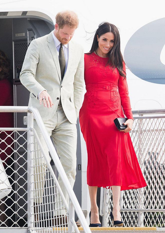Meghan had a quick change on the plane and arrived Tonga wearing a red midi-length dress by Self Portrait paired with a black clutch and pumps. Photo: Getty