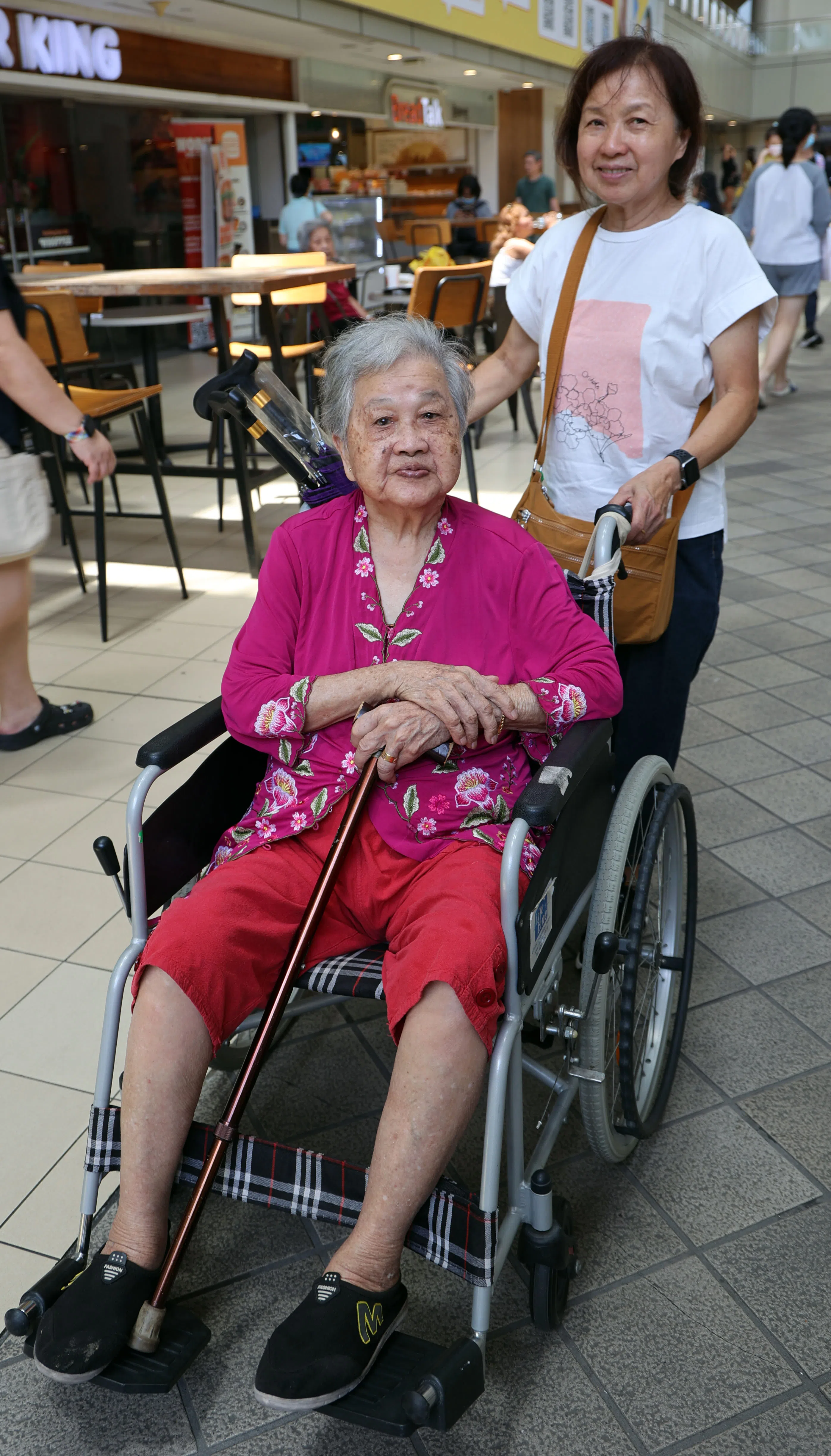 何女士推着坐轮椅的母亲，曾在路边等德士等了半个小时无果。（曾美玲摄）